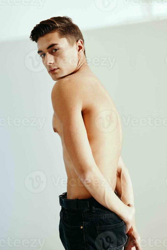 Sexy man in dark trousers on a light background naked torso photo