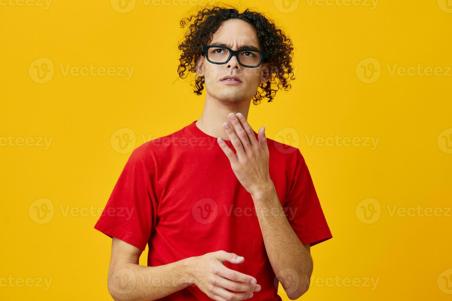 Lovely myopic young student man in red t-shirt funny eyewear looks aside posing isolated on over yellow studio background. The best offer with free place for advertising. Education College concept photo