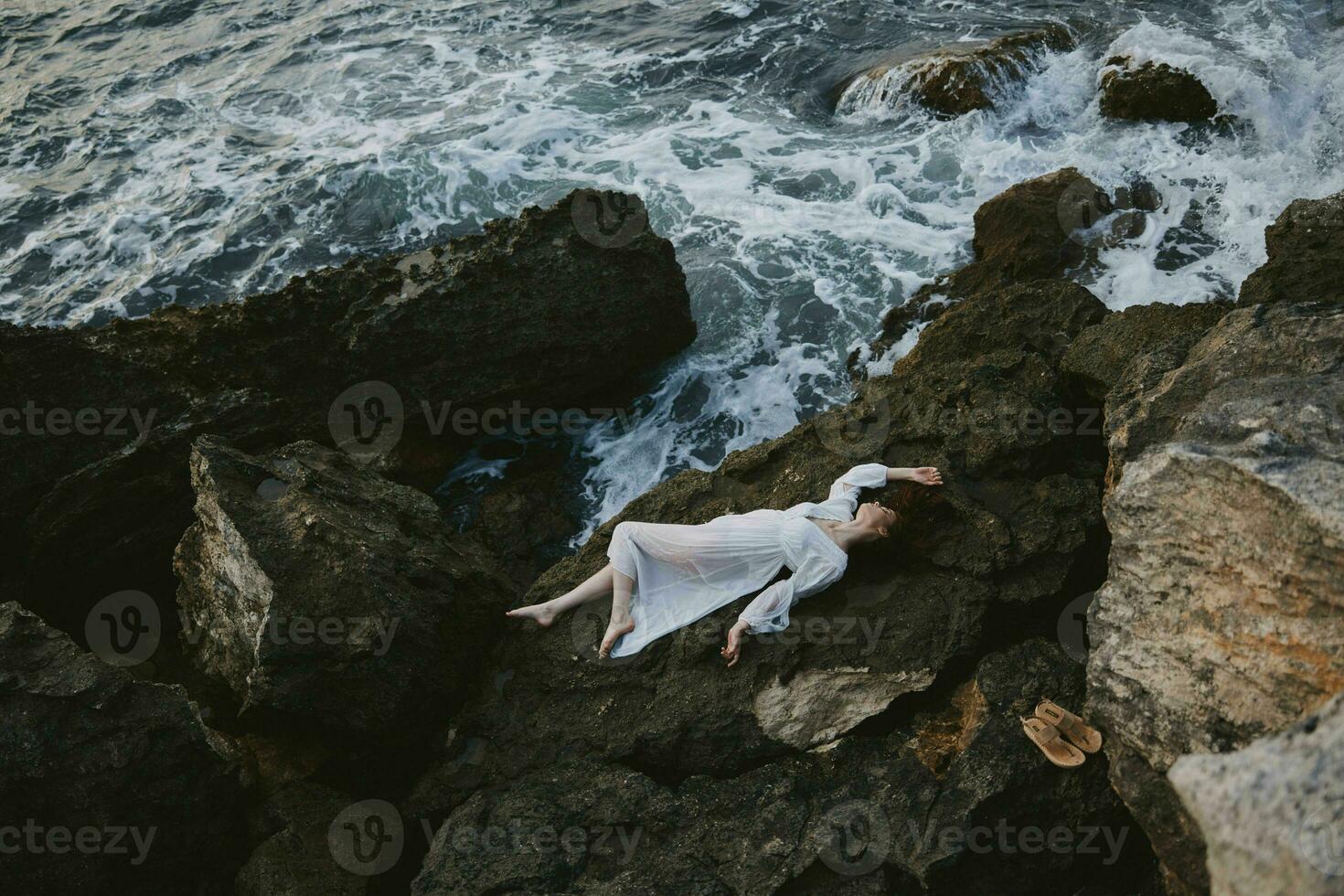 Beautiful bride lying on rocky coast with cracks on rocky surface Summer vacation concept photo