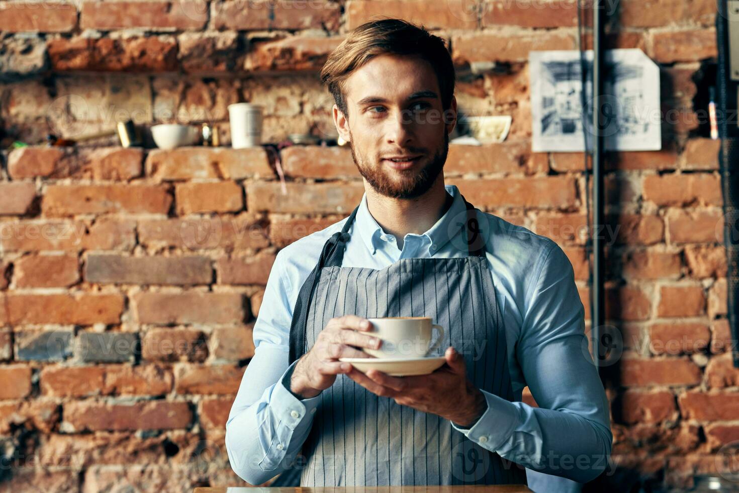 masculino camarero delantal café taza ladrillo pared restaurante Servicio foto