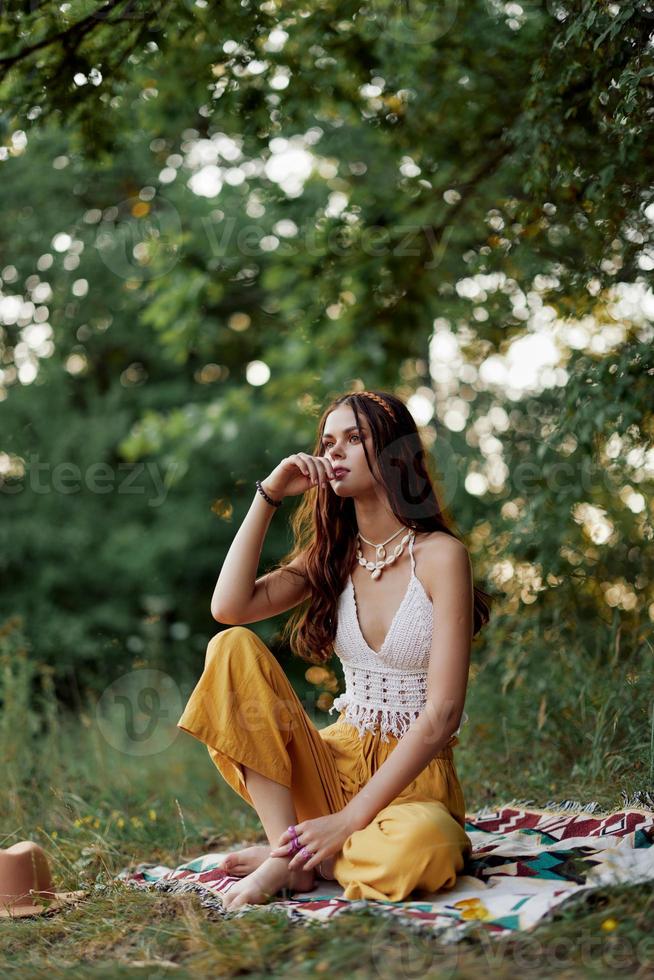 A young hippie woman meditates in nature in the park, sitting in a lotus position on her colorful plaid and enjoying harmony with the world in eco-clothing in the autumn photo