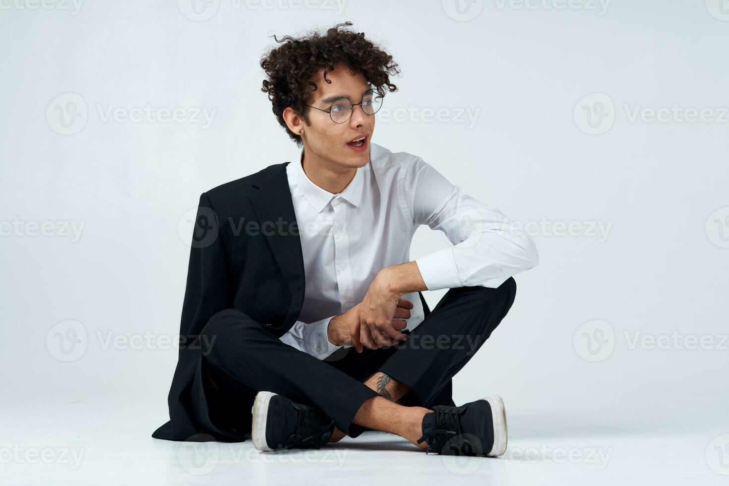 elegante joven hombre con Rizado pelo y en un clásico traje en un ligero antecedentes adentro en lleno crecimiento foto