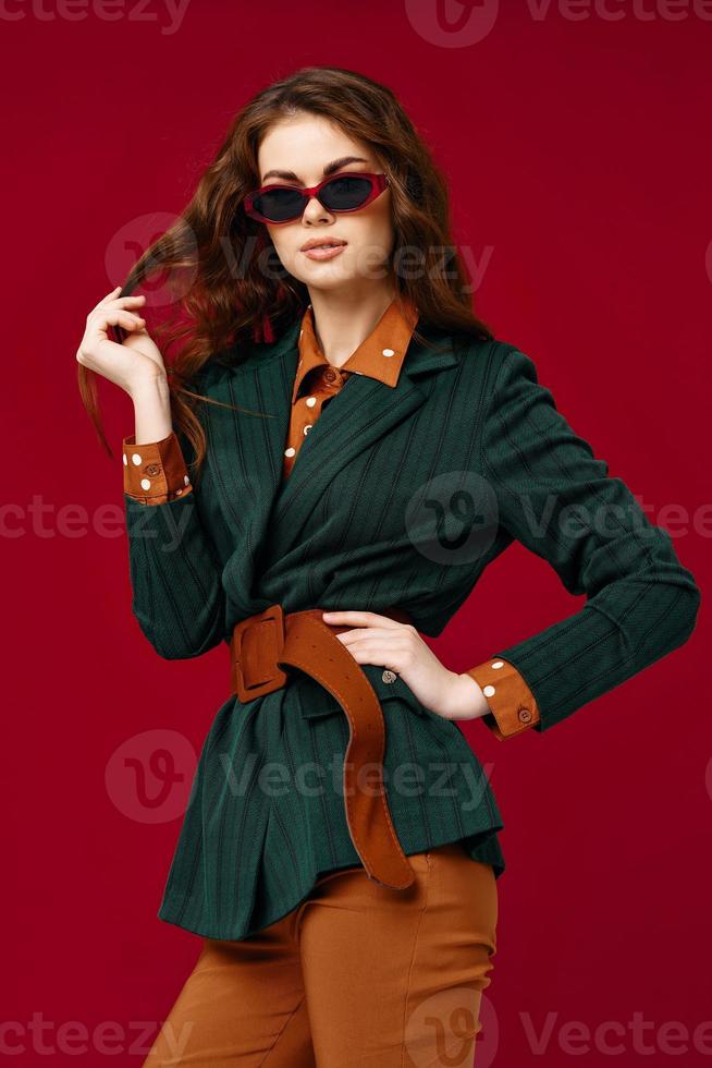 pretty woman holding hair fashionable suit and sunglasses luxury red background photo