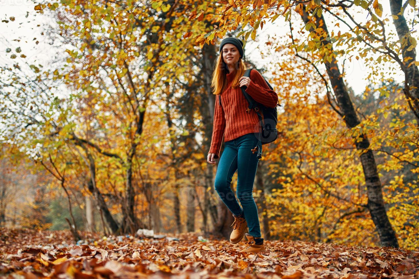 joven mujer en pantalones y un suéter con un mochila en su espalda camina en el parque en otoño en naturaleza, fondo ver foto