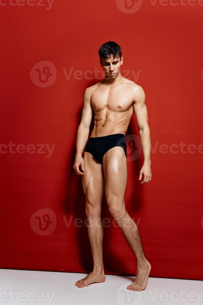 nude male bodybuilder in black panties on a red background photo