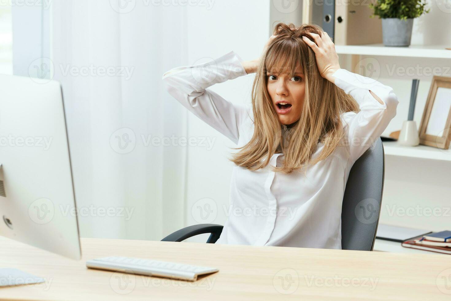 Shocked adorable blonde businesswoman typing answer for client look at camera touch head sitting at workplace in modern office. Unhappy employee work on computer online in support service. Copy space photo
