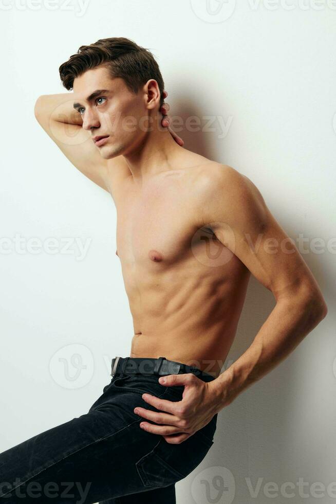 guy with a naked torso holds his hand behind his head side view dark pants photo