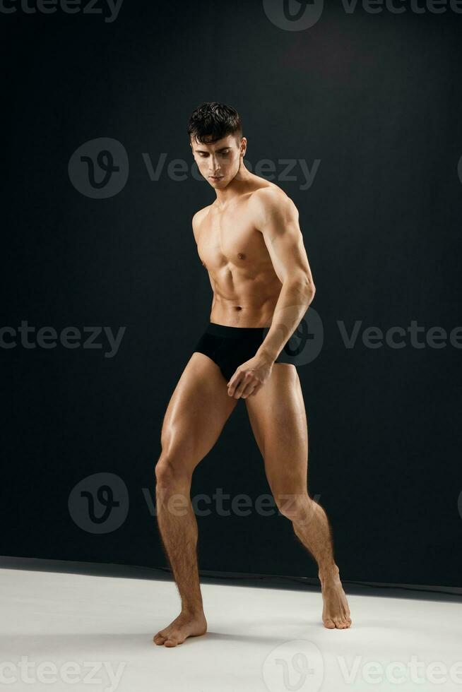 sexy man with naked muscular body in black panties dark background photo