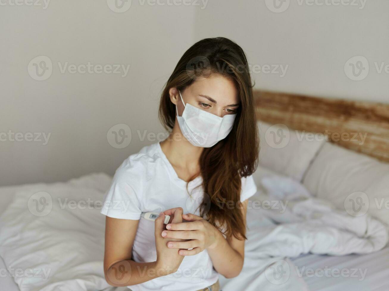 woman sitting in bed with thermometer under her arm checking