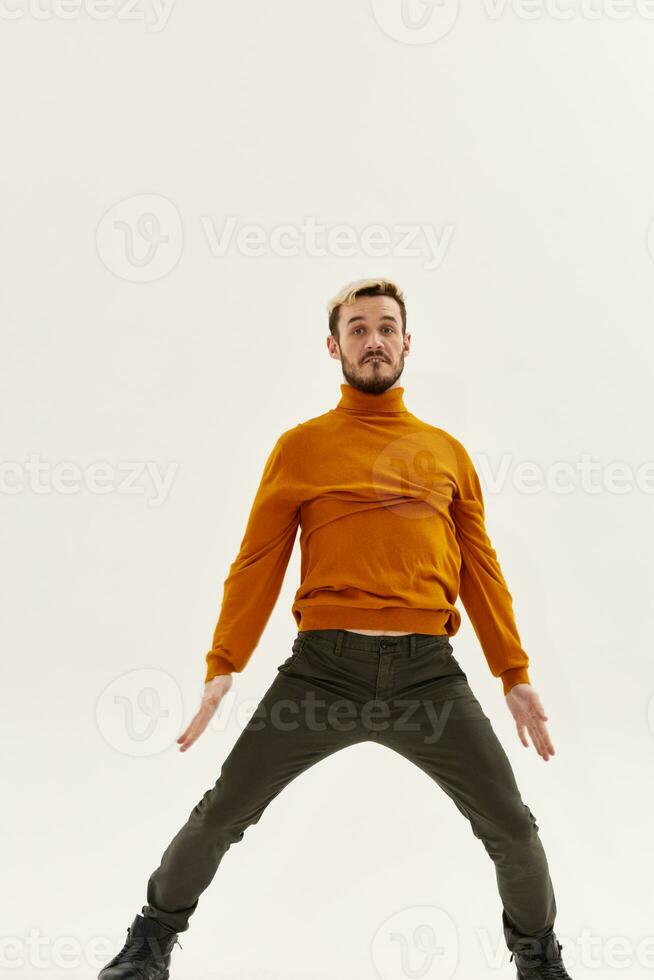 a man in an orange sweater spread his legs shoulder-width apart and gestures with his hands photo