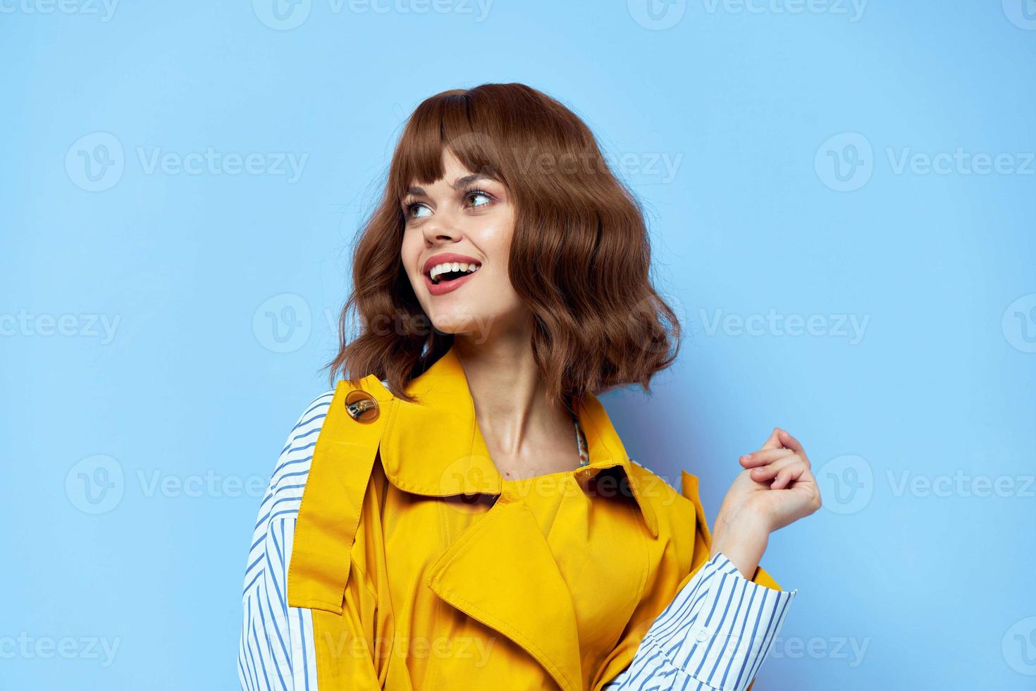 Happy woman in yellow coat looks to the side over blue background and smiling cropped view. photo