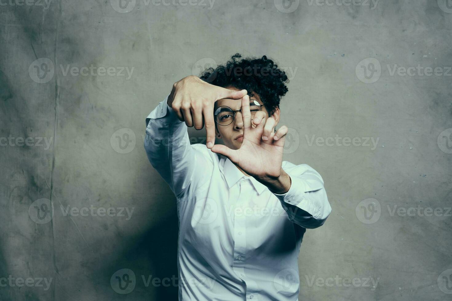 de moda chico con Rizado pelo gesticulando con su manos en un gris antecedentes retrato de cerca foto