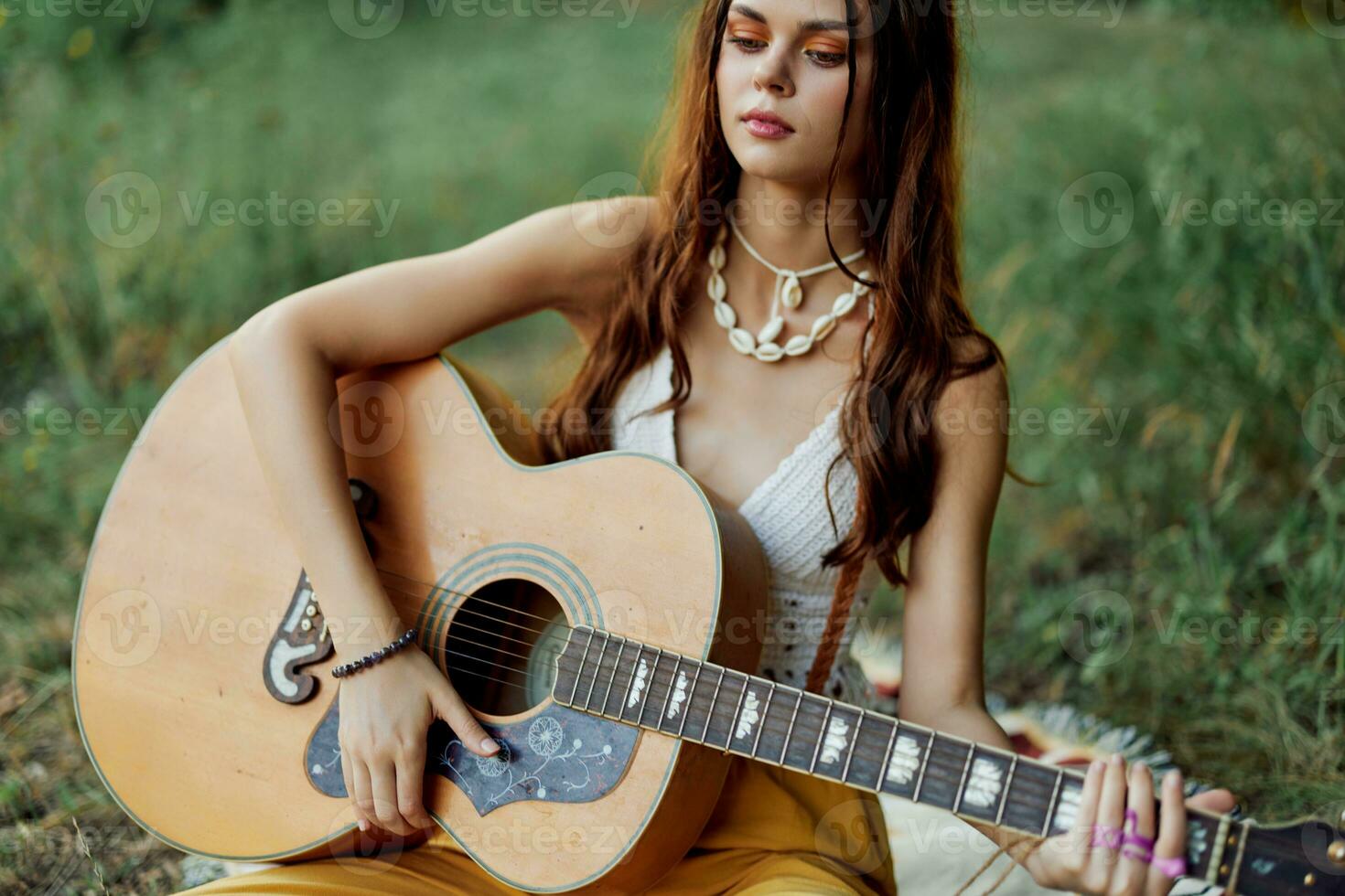 hippie mujer sonriente y abrazando su guitarra en naturaleza en el parque en el puesta de sol ligero foto