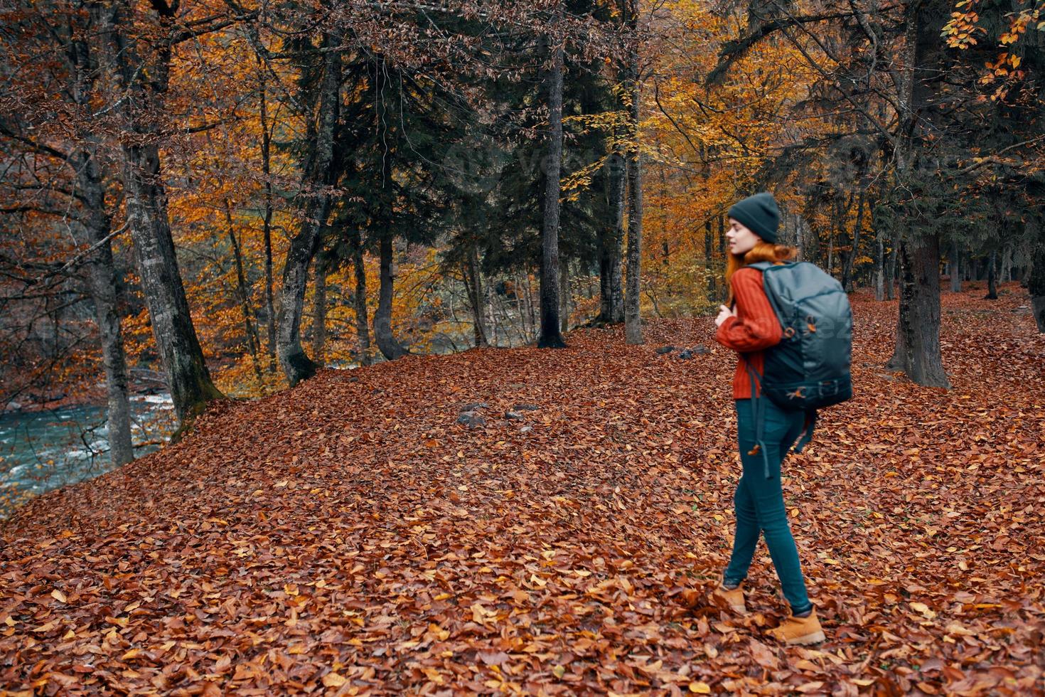 mujer con mochila excursionismo viaje en otoño parque alto arboles río caído hojas foto