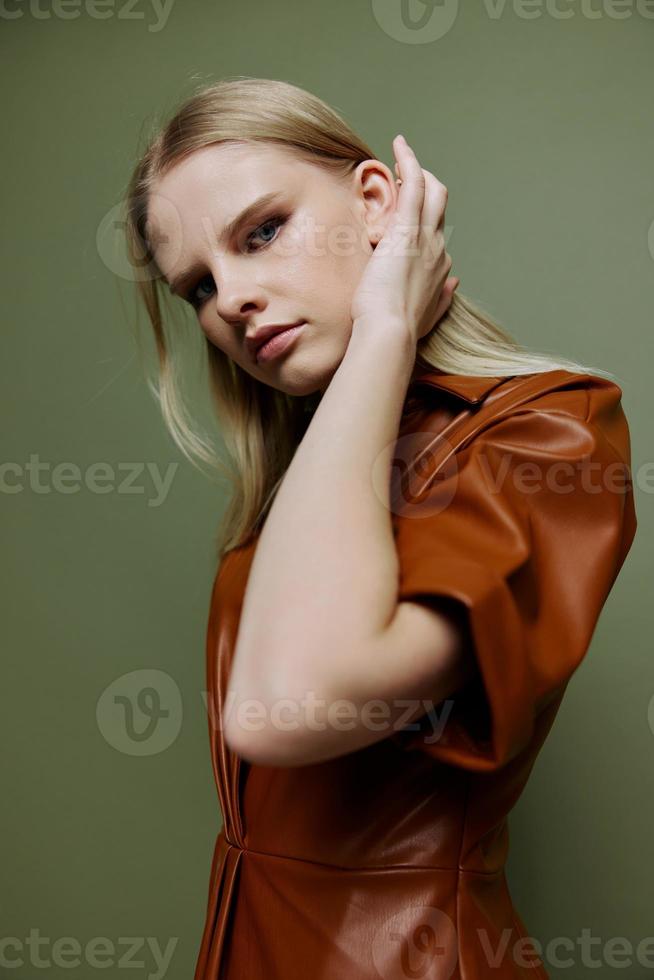Stylish closeup portrait for banner design. Sexy blonde female in leather brown palette clothes looks over her shoulder at camera posing isolated on over green studio background photo