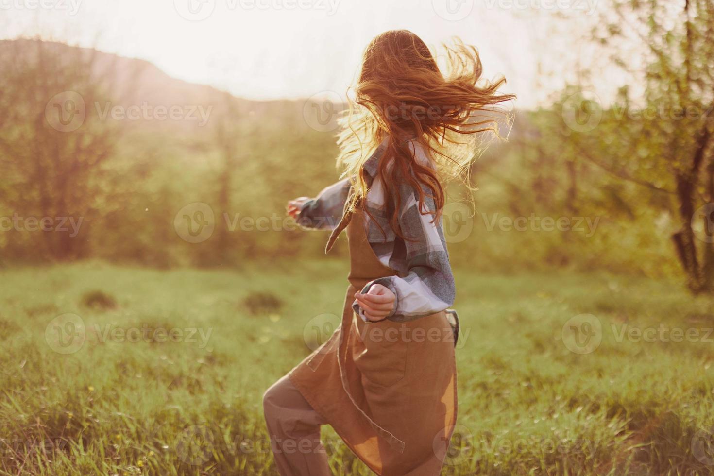 un mujer corriendo mediante un campo en un verano día con largo fluido pelo en el rayos de el ajuste Dom. el concepto de libertad y armonía con naturaleza foto