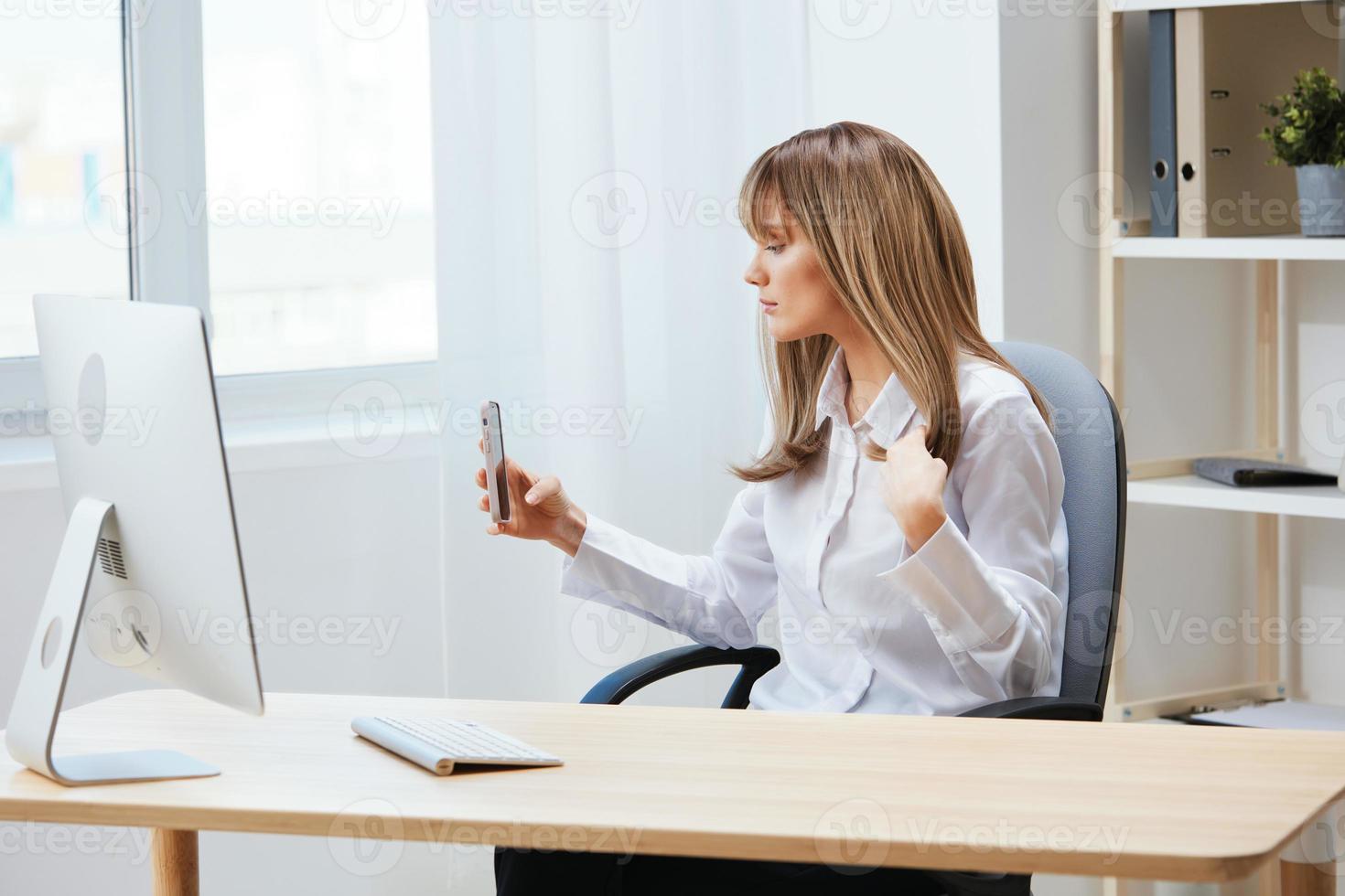Serious adorable blonde businesswoman worker freelancer look at phone doing selfie in light modern office. Employee work doing have video call record live in social media. Copy space photo