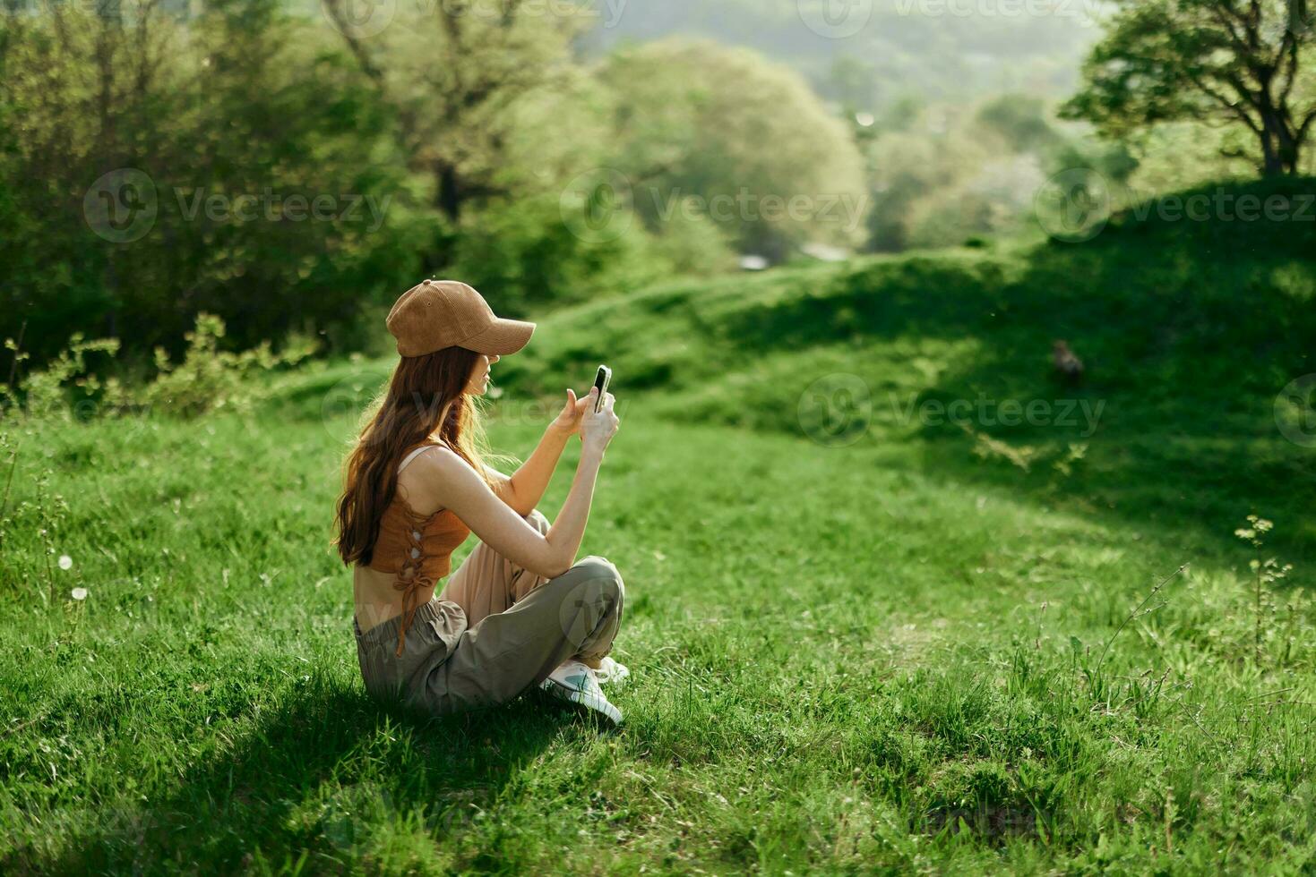 A woman sitting on the green grass in a park in summer against a landscape of trees, the work of a freelancer and blogger photo