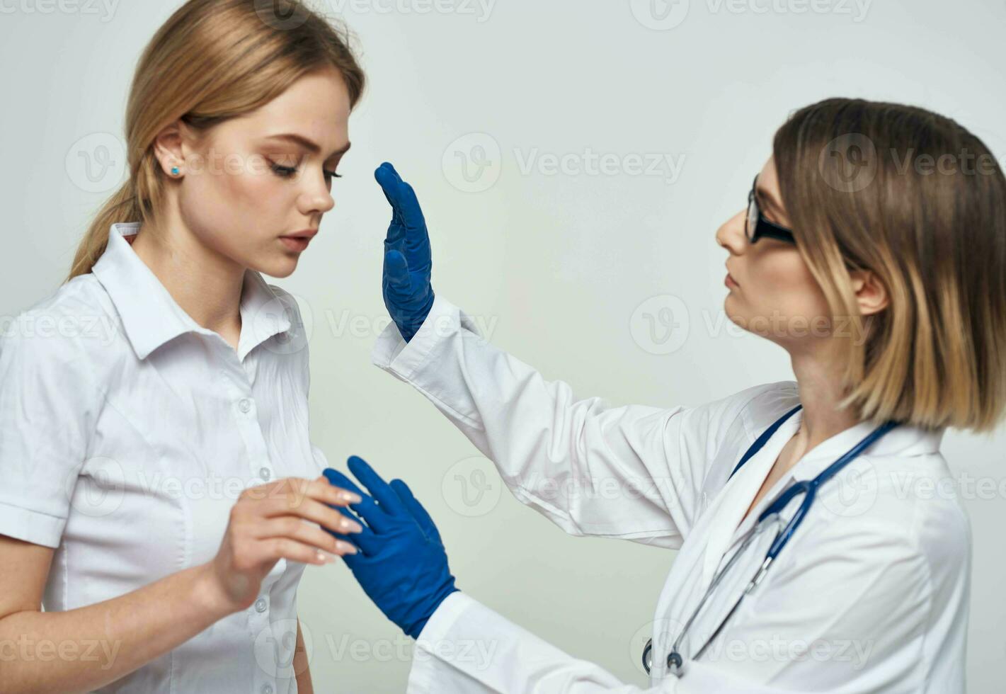 Woman doctor in a medical gown and in blue gloves with a stethoscope around her neck and a female patient photo