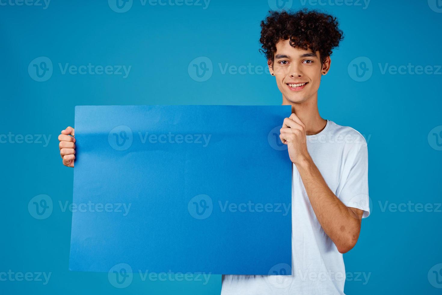 Cheerful guy with curly hair and blue mockup poster advertising photo