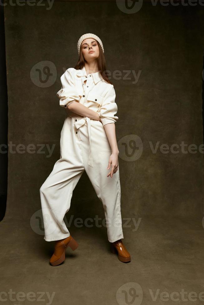 fashionable woman in hat jumpsuit and brown shoes lifted her leg up on brown background photo