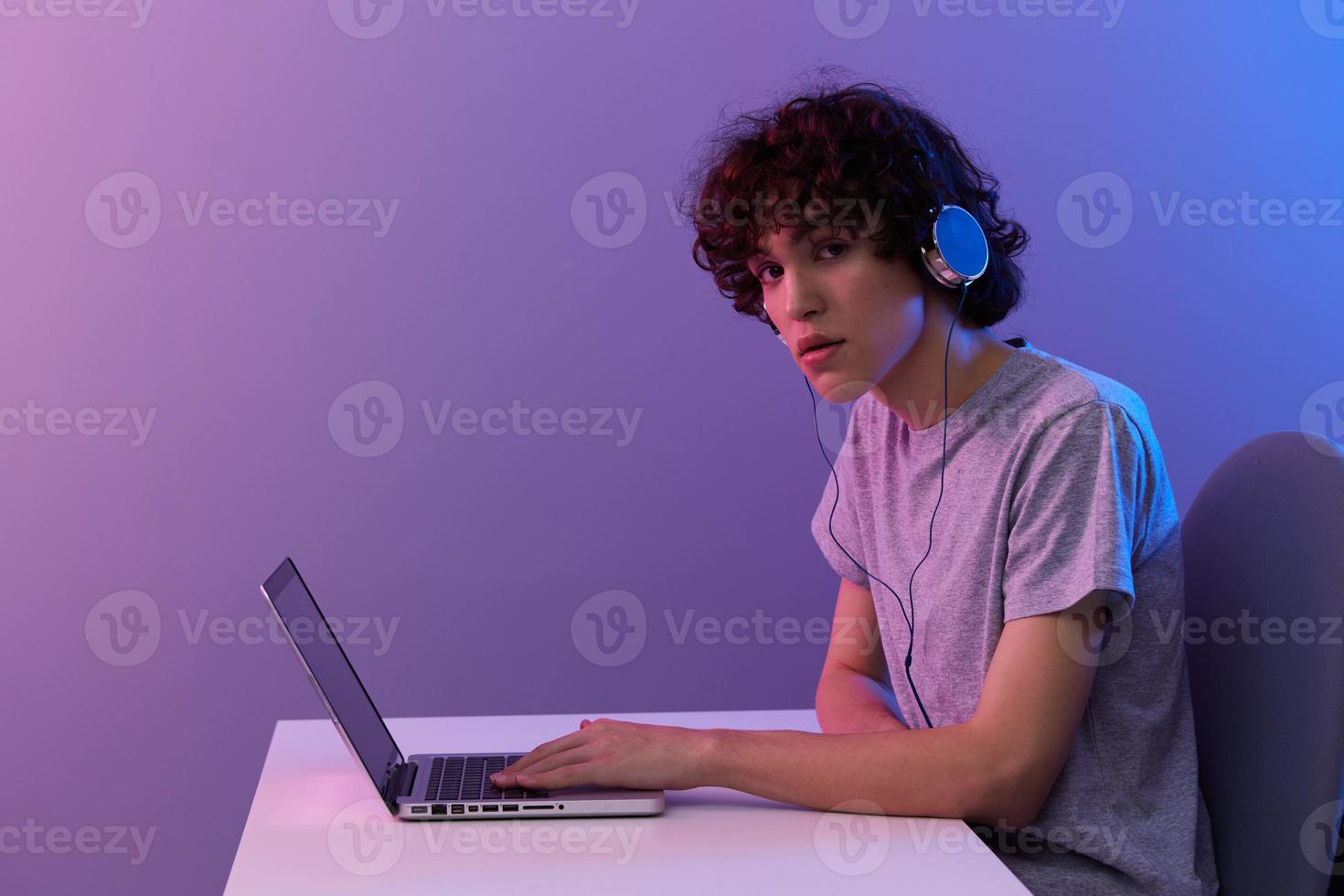 curly guy cyberspace playing with headphones in front of a laptop violet background photo