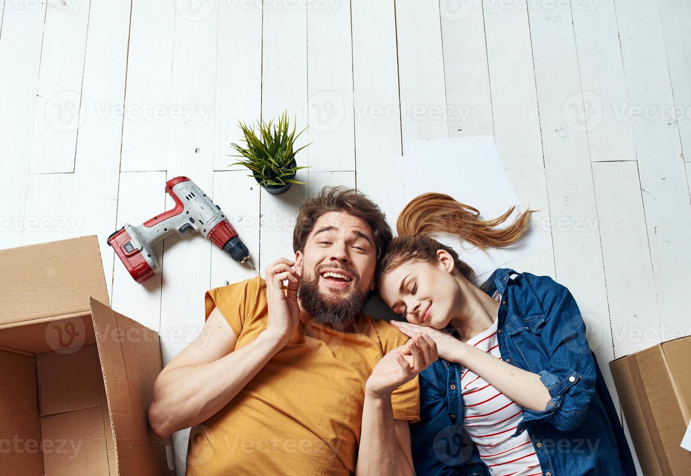 hombre y mujer con cajas alrededor mentira en el piso Moviente flor en un maceta reparar trabajo foto