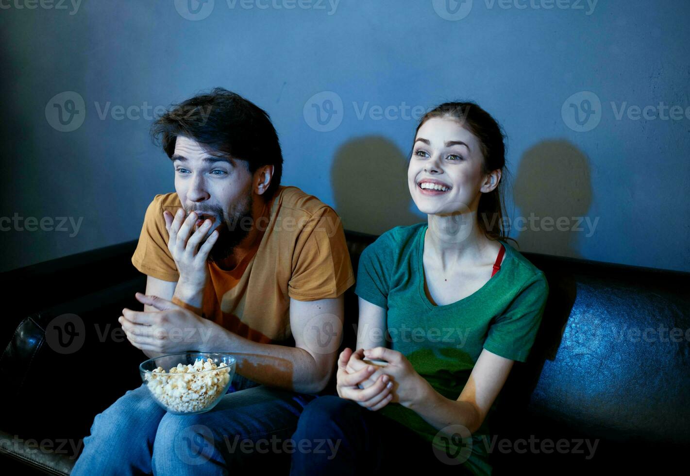 Scared man and happy woman watching TV in the evening on the couch photo