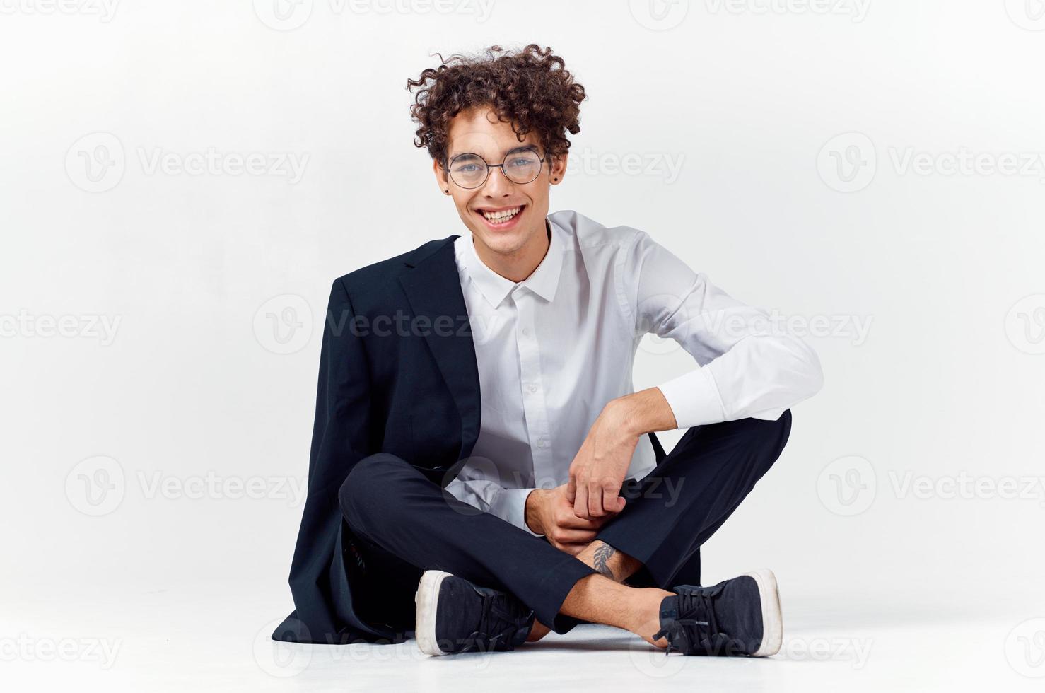 elegante joven hombre con Rizado pelo y en un clásico traje en un ligero antecedentes foto