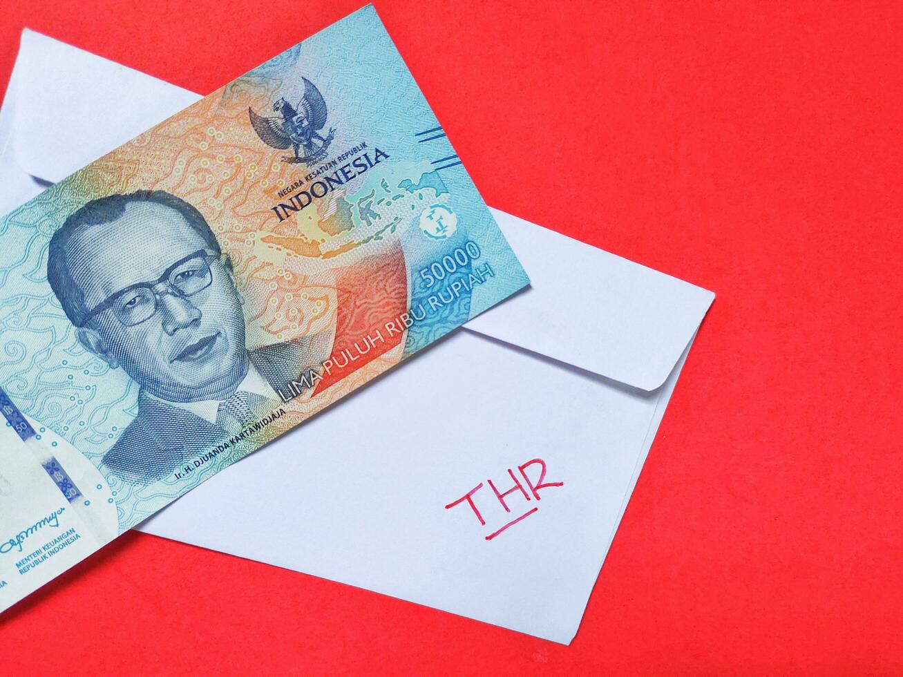 A white envelope written of THR and new Indonesian banknotes, usually Tunjangan Hari Raya or called THR are given to employees ahead of Eid. Top view photo
