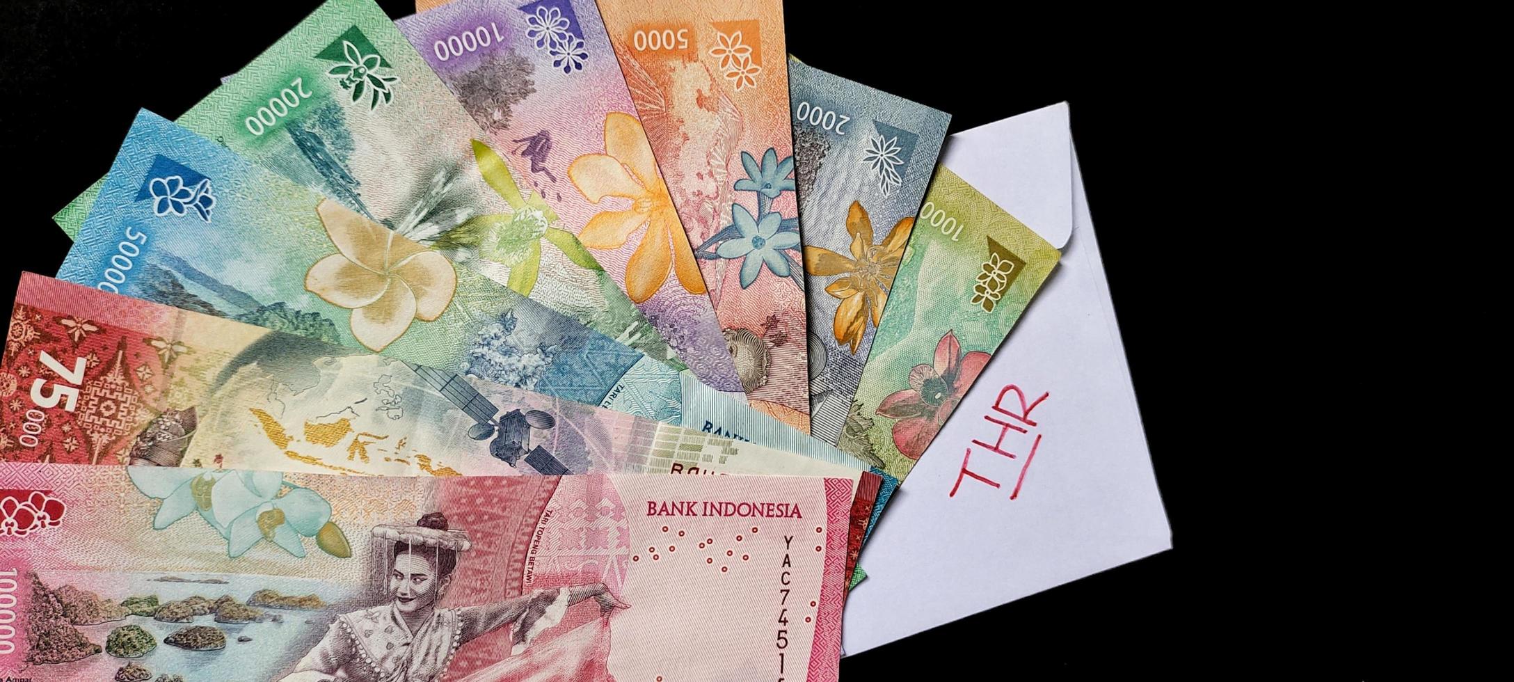 New banknotes issued in 2022 from Rp.1,000 to Rp.100,000. Indonesian rupiah currency with a white envelope labeled THR. Tunjangan Hari Raya concept photo