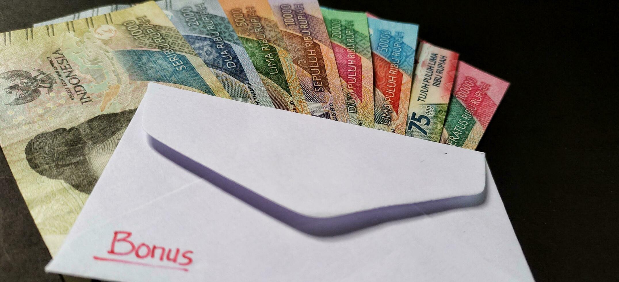 New banknotes issued in 2022 from Rp.1,000 to Rp.100,000. Indonesian rupiah currency with a white envelope labeled Bonus. Tunjangan Hari Raya concept, close up view photo