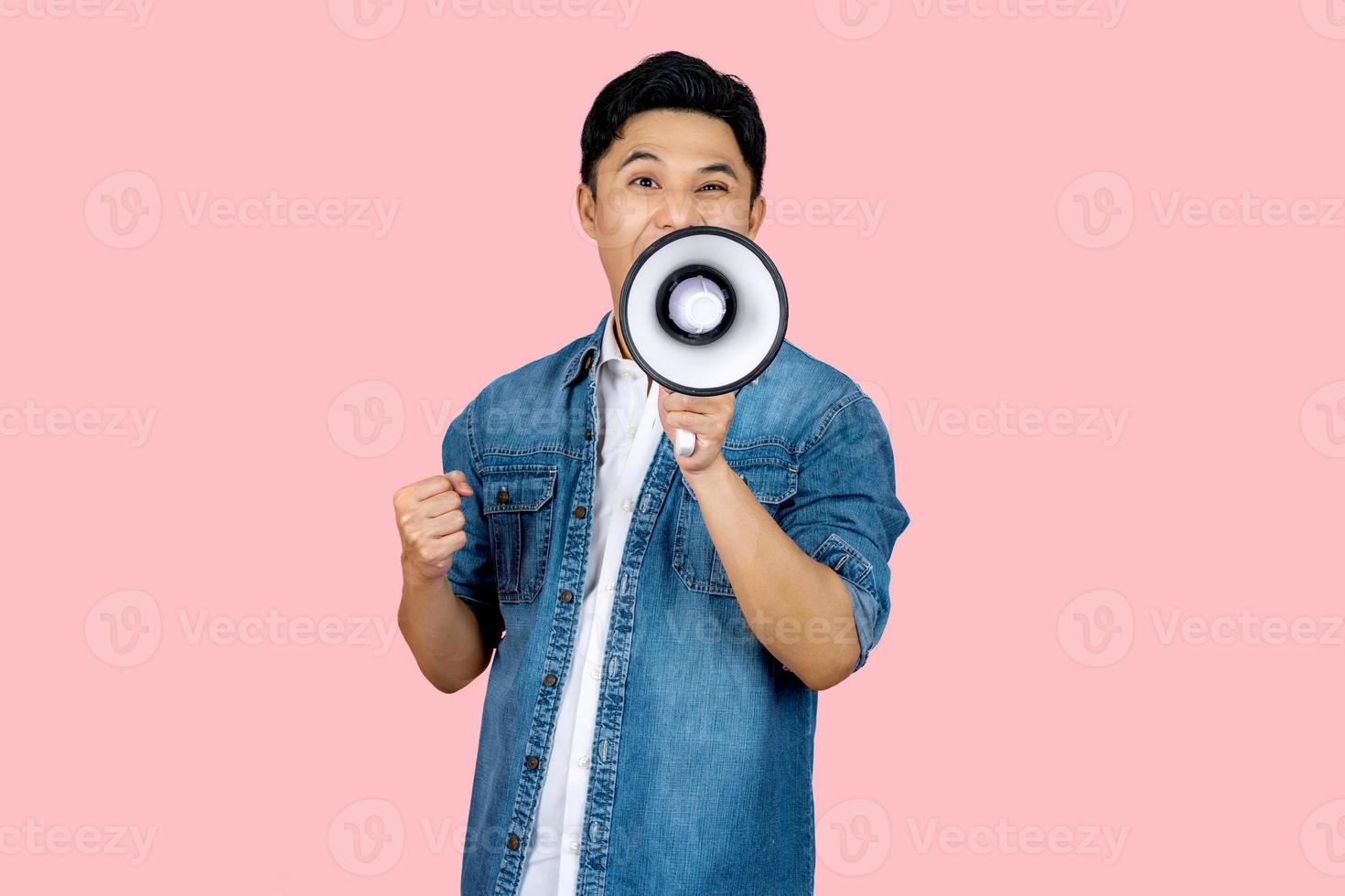 Happy asian man in casual shirt t-shirt scream in megaphone shout and showing triumph gesture on workspace isolated on pink  background. People lifestyle concept. photo