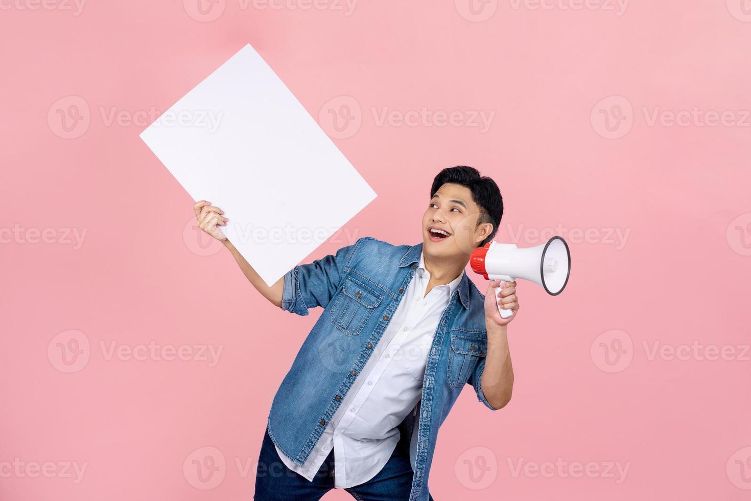 Smiling happy Asian man shouting announce into megaphone and holding blank speech bubbles on pink background. photo