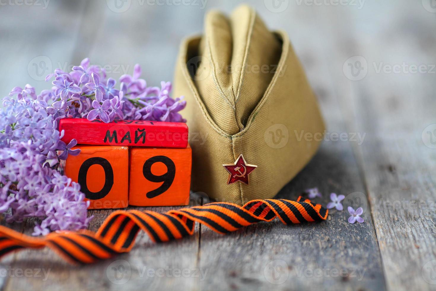 Wooden calendar with Russian text May 9, garrison cap, george ribbon and a bouquet of lilacs on a wooden background. Victory Day. photo