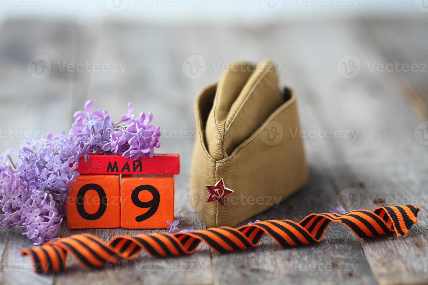 Wooden calendar with Russian text May 9, garrison cap, george ribbon and a bouquet of lilacs on a wooden background. Victory Day. photo