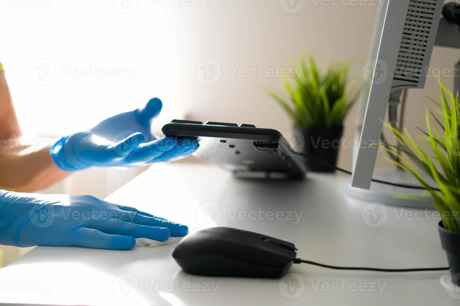 masculino manos en caucho guantes limpiar el blanco mesa y teclado desde el computadora. desinfección en el oficina durante el covid-19 pandemia. foto