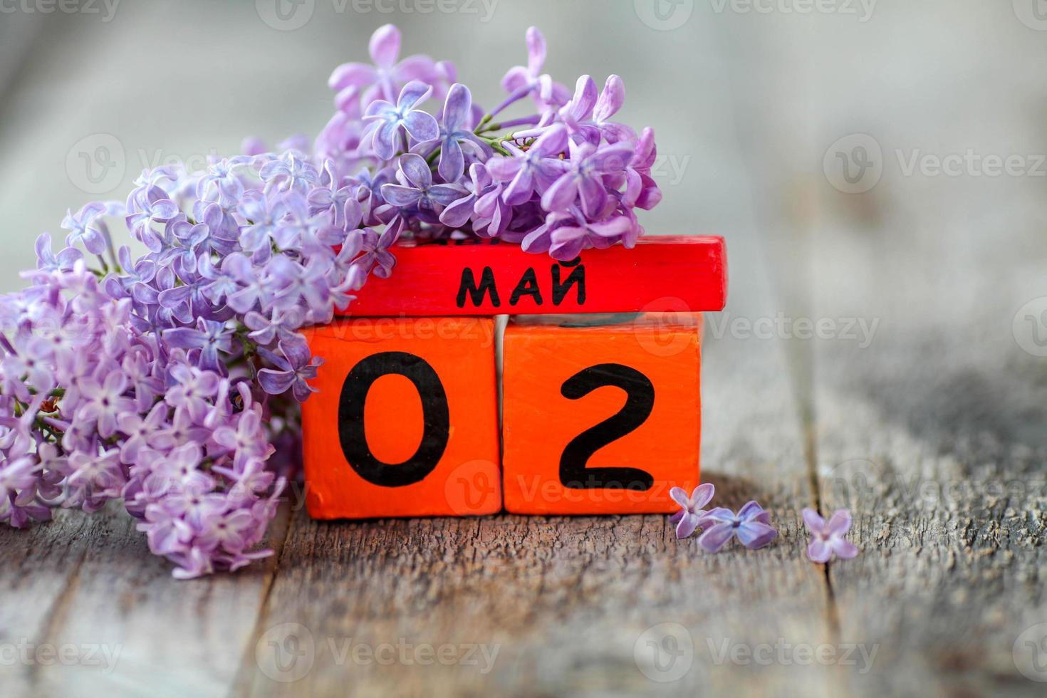 de madera calendario con ruso texto mayo 2 y un ramo de flores de lilas en un de madera antecedentes. Copiar espacio. foto