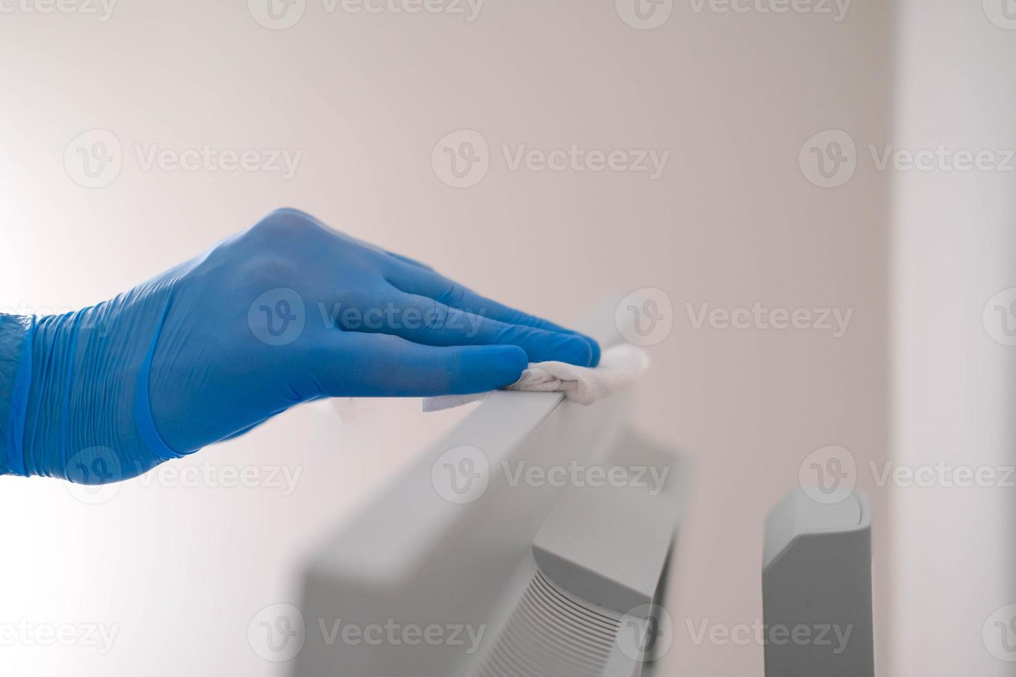 A male hand in rubber gloves wipes the dust from a computer monitor with a napkin. Disinfection at home, cleaning in the context of the COVID-19 pandemic. photo