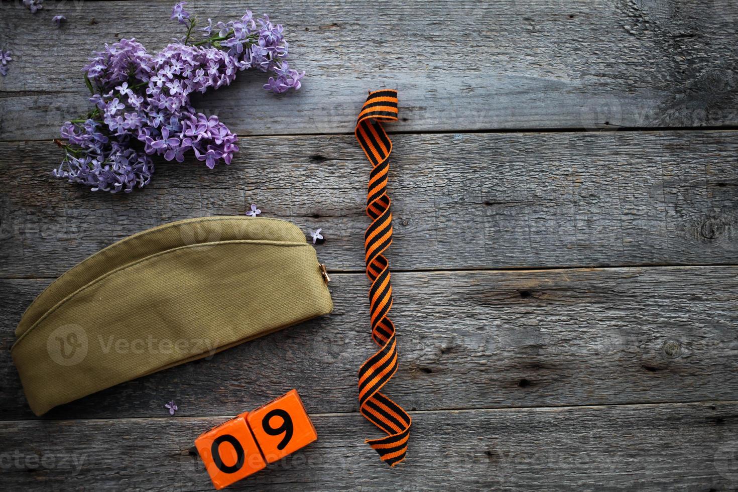 Flask, george ribbon, garrison cap and lilacs on a wooden background. Wooden calendar with date 9 May. Victory Day. Copy space. photo