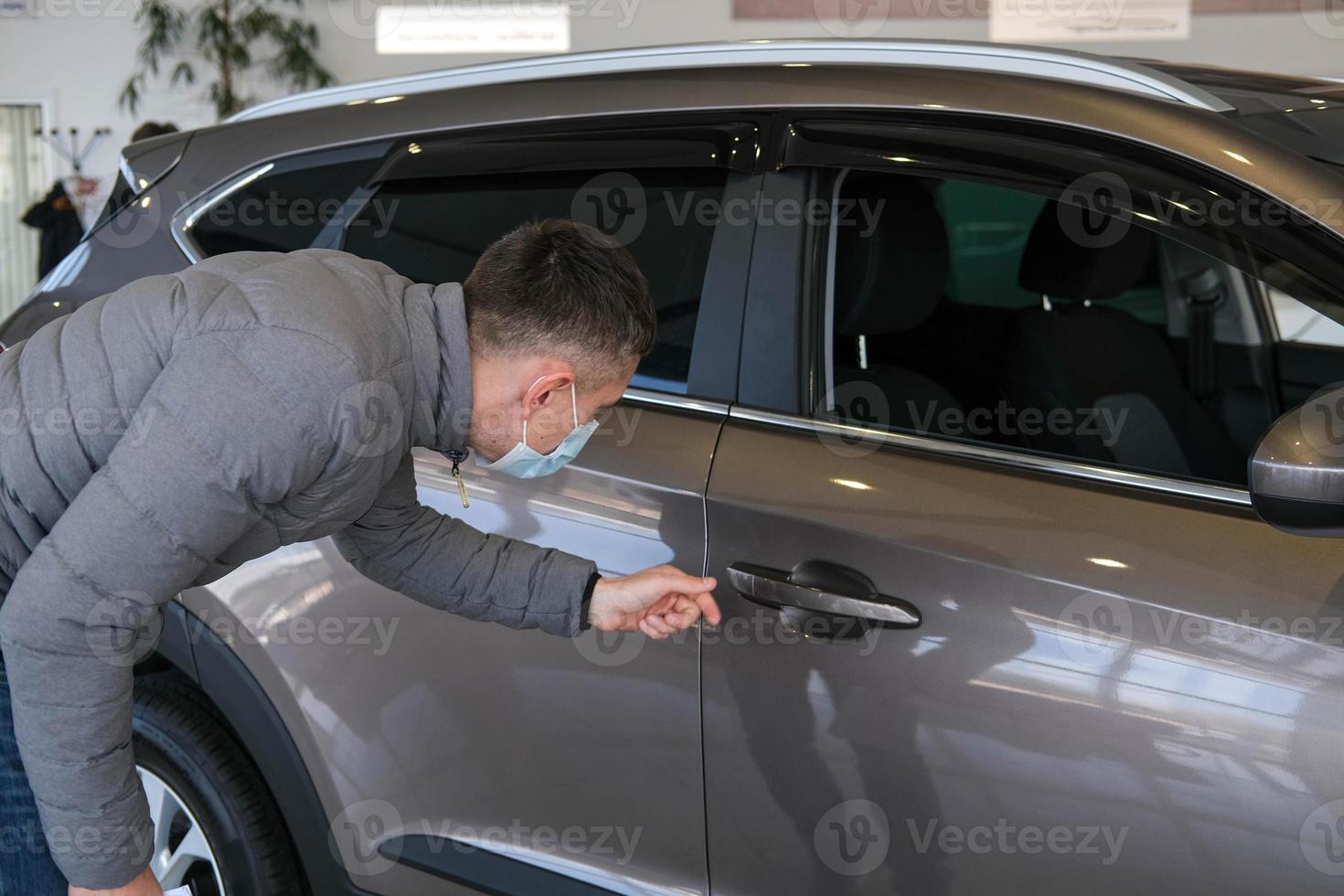 A man in a medical mask examines a car in the cabin for defects. Car rent. Buying a car photo