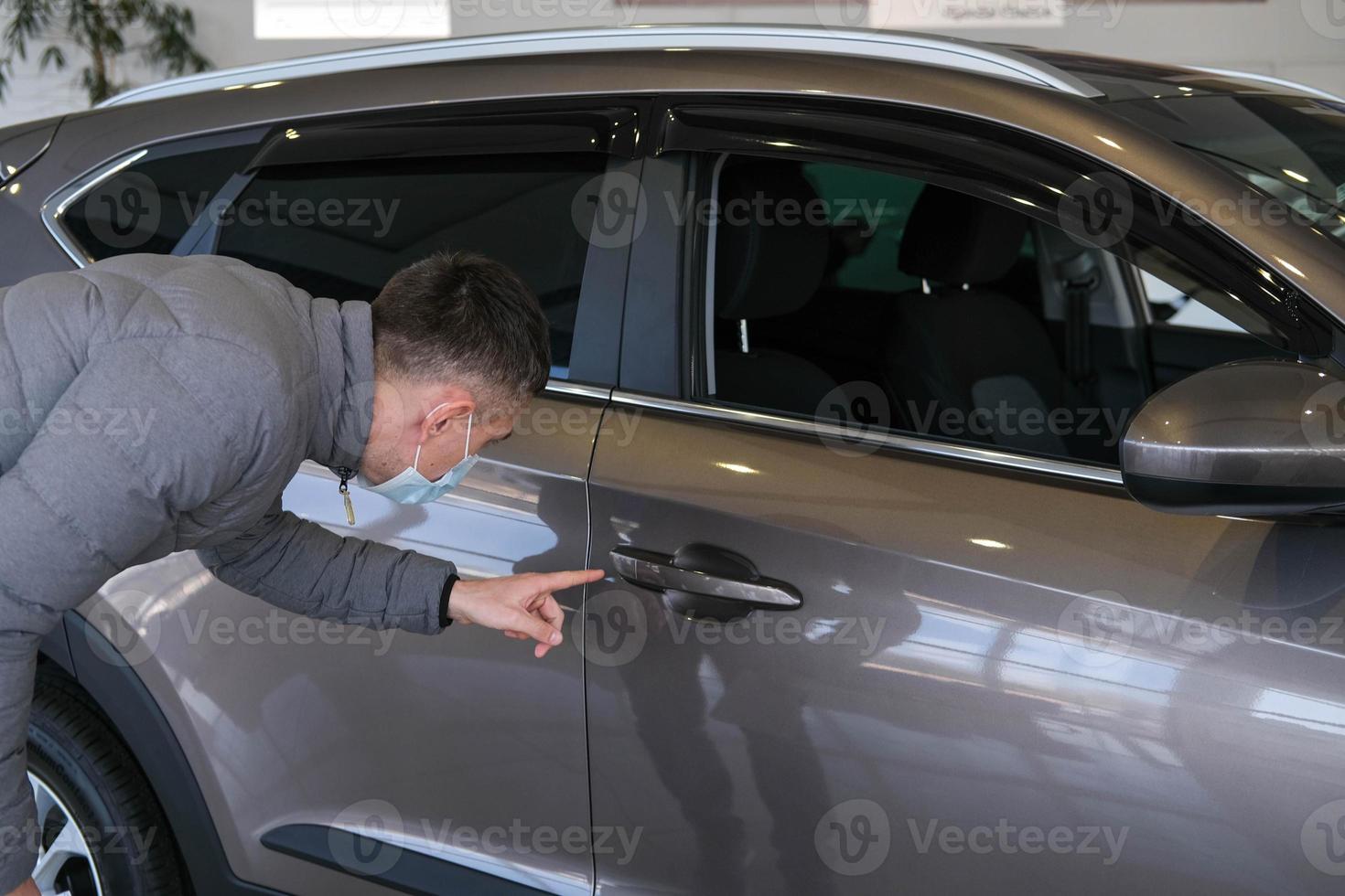 A man in a medical mask examines a car in the cabin for defects. Car rent. Buying a car photo