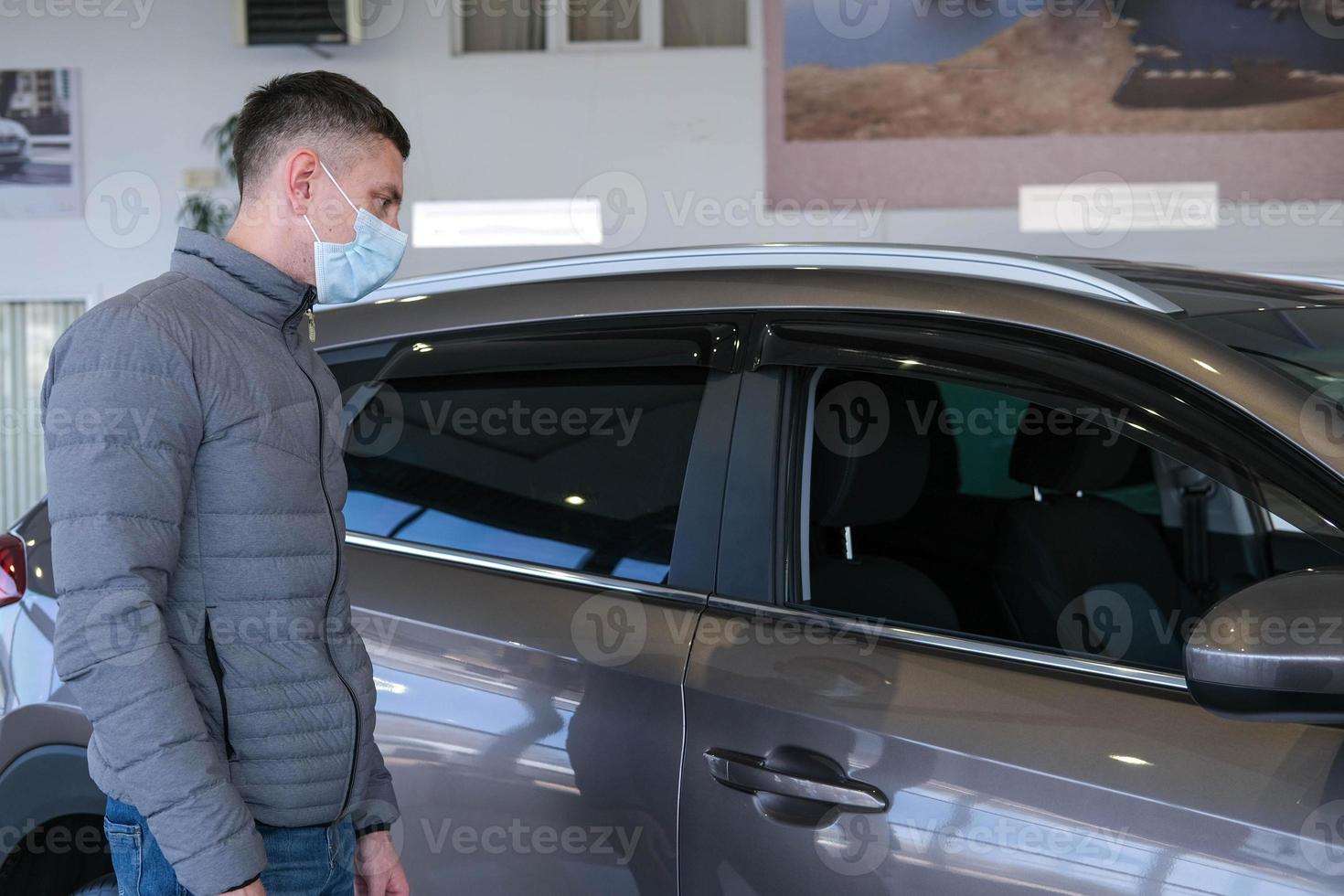 A man in a medical mask examines a car in the cabin for defects. Car rent. Buying a car photo