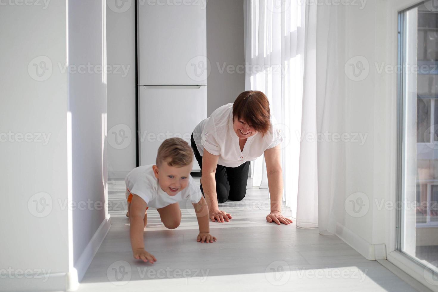 Grandmother and her grandson are crawling on the floor, playing catch-up. The nanny plays merrily with a small child. photo