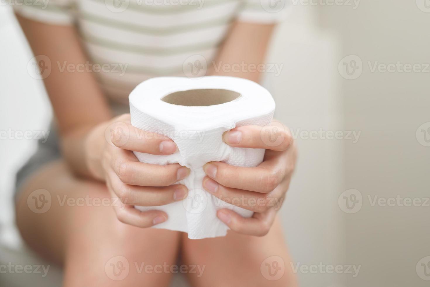 retrato de un mujer sufre desde Diarrea su estómago doloroso. dolor y problema. mano sostener pañuelo de papel papel rodar en frente de baño bol. estreñimiento en baño. higiene, salud cuidado concepto. foto