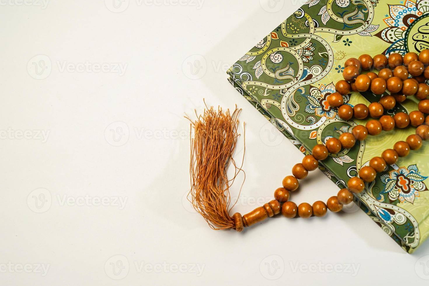 The Holy Al Quran with written arabic calligraphy meaning of Al Quran and rosary beads or tasbih on white background with copy space. photo