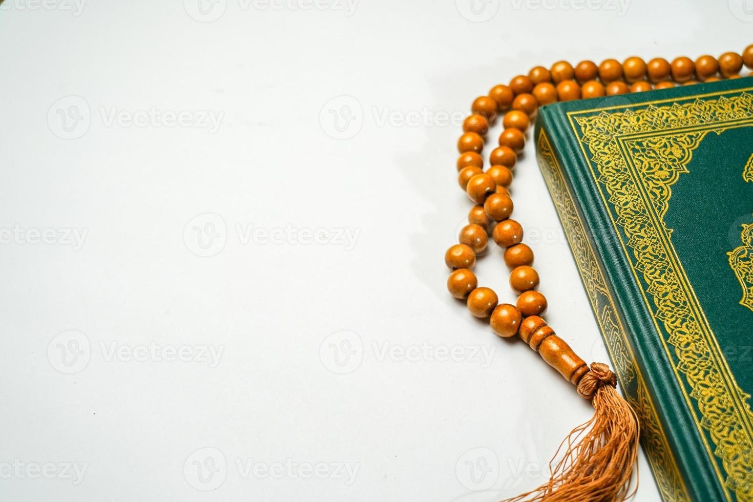 The Holy Al Quran with written arabic calligraphy meaning of Al Quran and rosary beads or tasbih on white background with copy space. photo