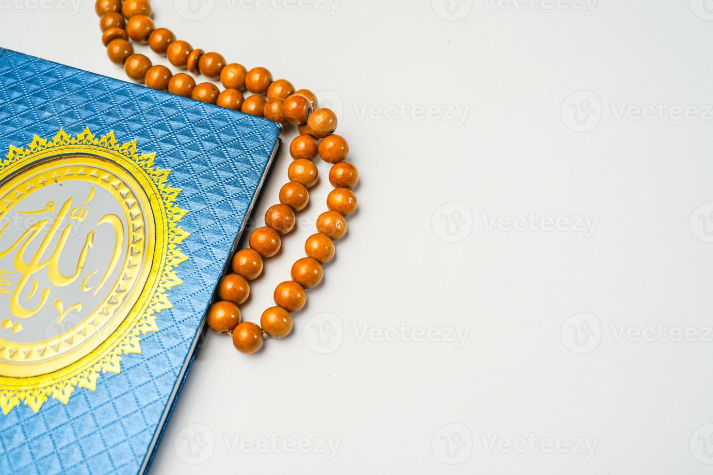 The Holy Al Quran with written arabic calligraphy meaning of Al Quran and rosary beads or tasbih on white background with copy space. photo