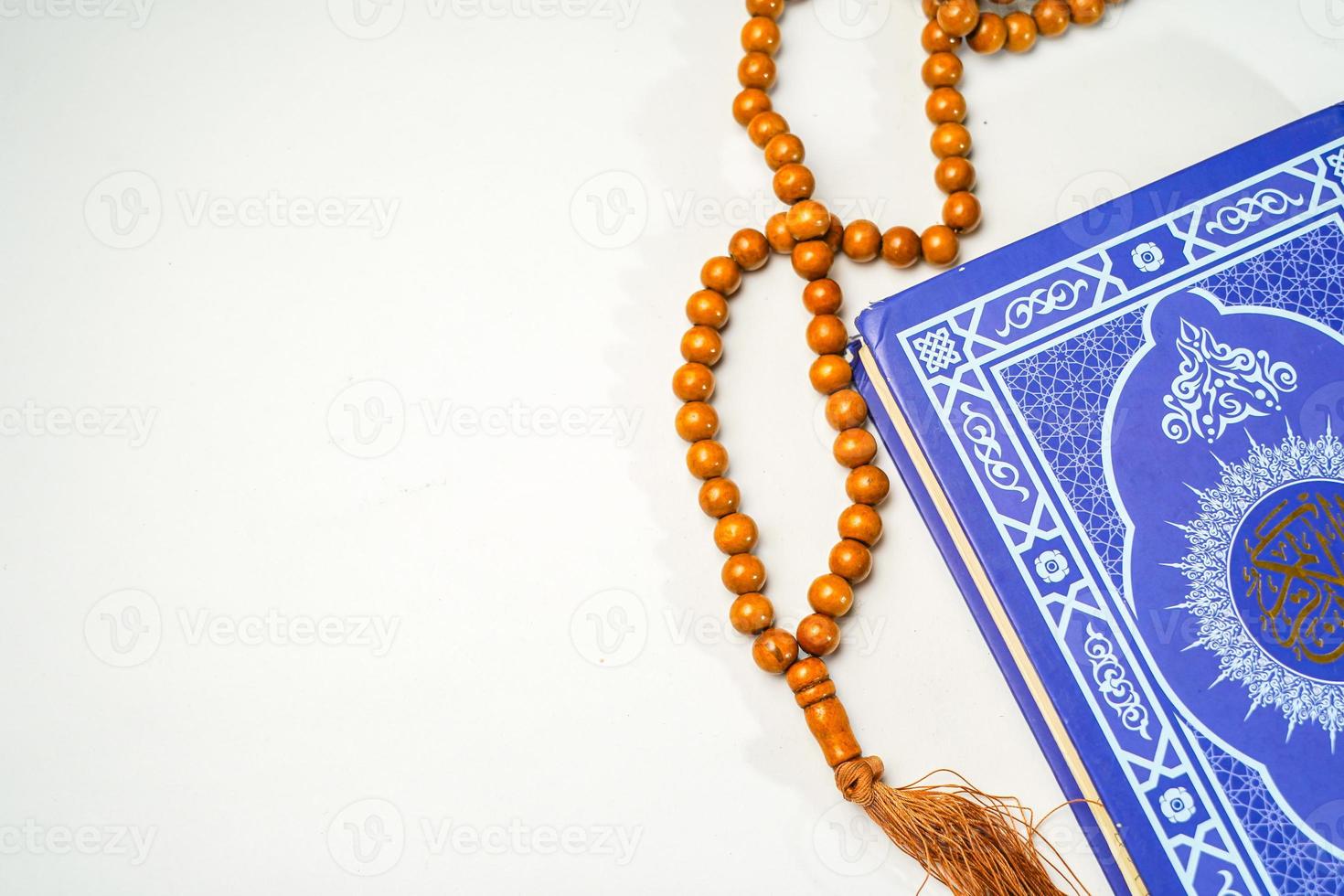 The Holy Al Quran with written arabic calligraphy meaning of Al Quran and rosary beads or tasbih on white background with copy space. photo