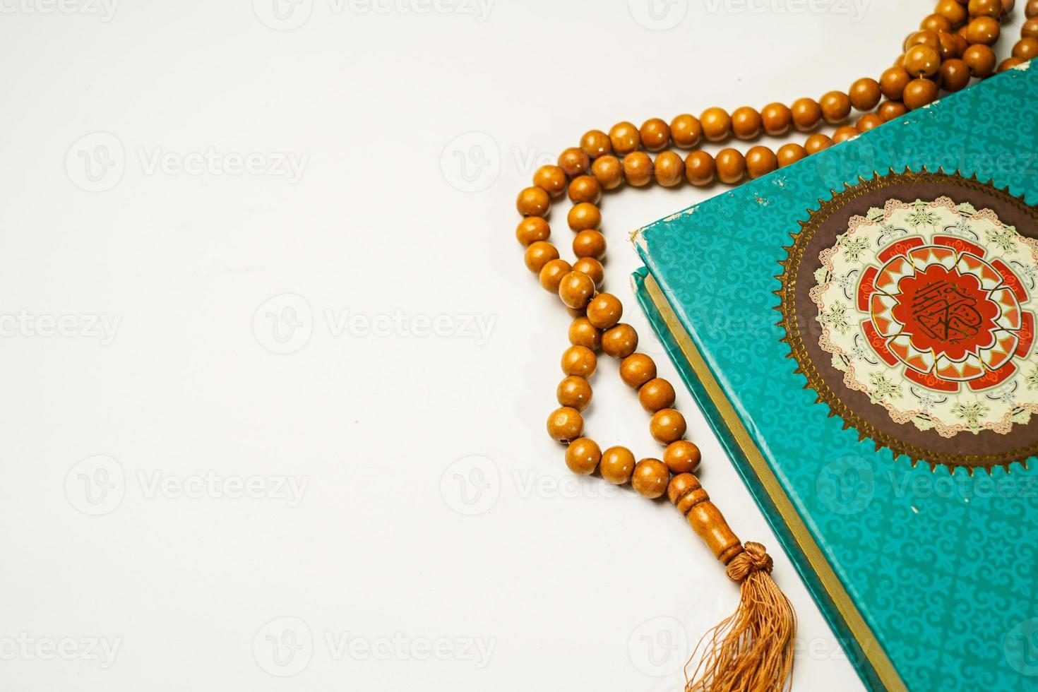 The Holy Al Quran with written arabic calligraphy meaning of Al Quran and rosary beads or tasbih on white background with copy space. photo
